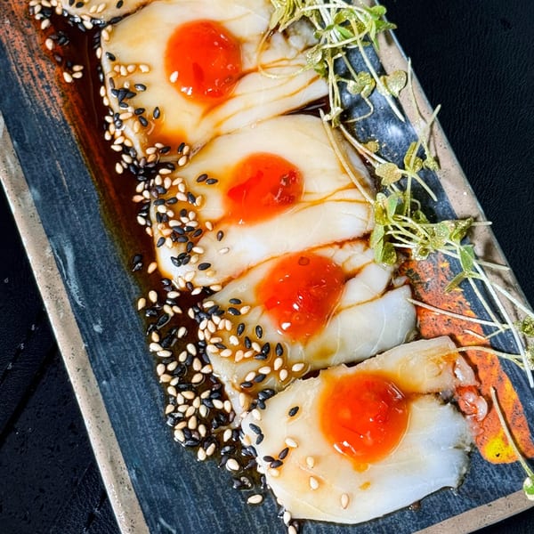 Temak House Florida's Japanese dish with white fish, red sauce, sesame seeds, and microgreens on a dark plate.