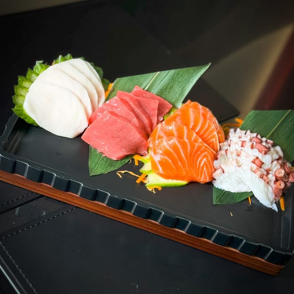 A black tray holds various sashimi: white fish, tuna, salmon, and octopus, garnished with greens.
