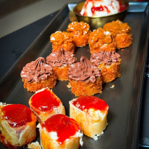 A tray of sweet sushi rolls with chocolate, caramel, and strawberry toppings, plus a bowl of ice cream.